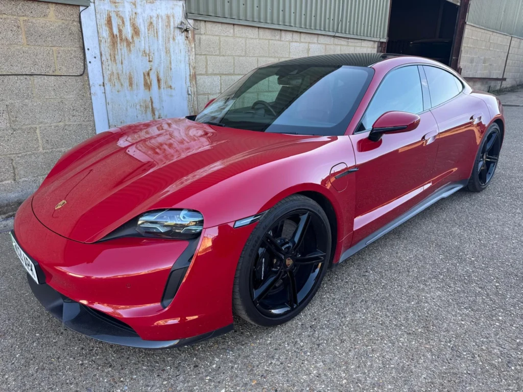 Red Porsche Taycan electric sports saloon outside an industrial building
